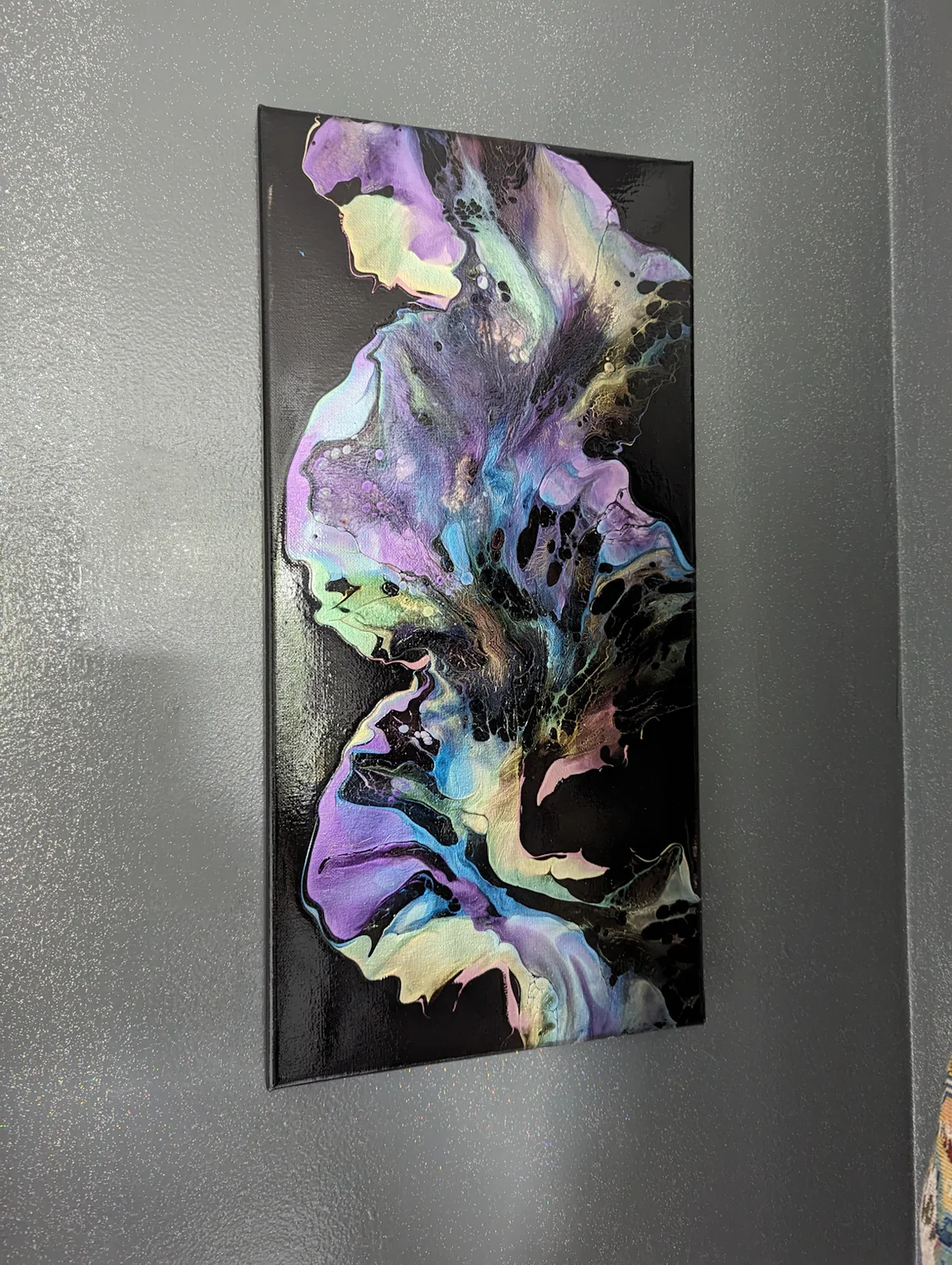 A tall purple, green and black painting displayed on a gray wall.