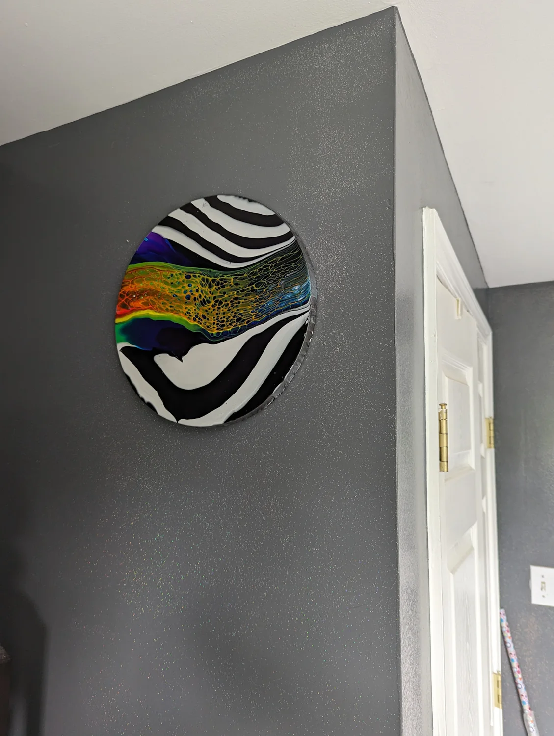 A circular zebra-striped and rainbow painting displayed near a doorway.