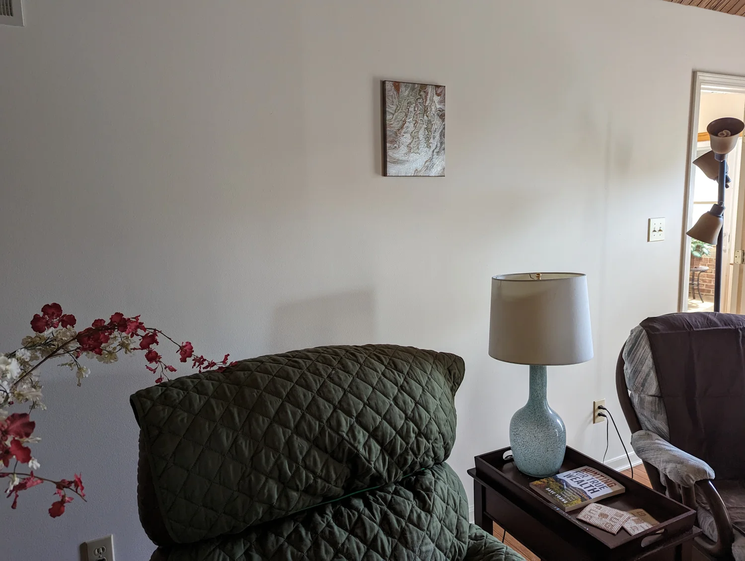 A small pale abstract painting displayed above a chair in a living room.